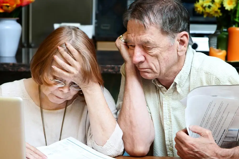 An elderly couple looking stressed while reviewing medical bills and financial documents.